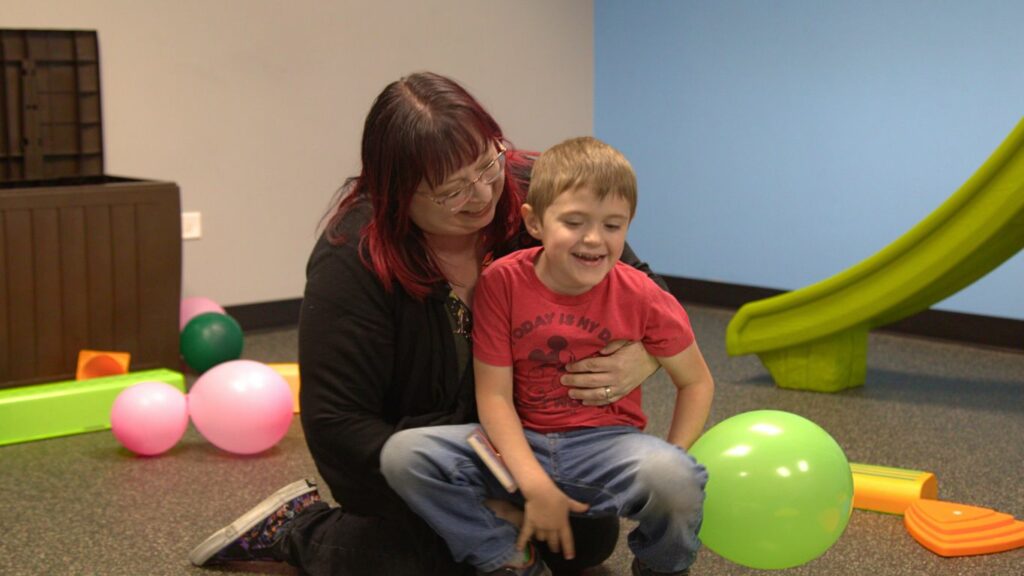 ABA therapy being performed with a young child and RBT therapist in a bright room with sensory toys and balloons.
