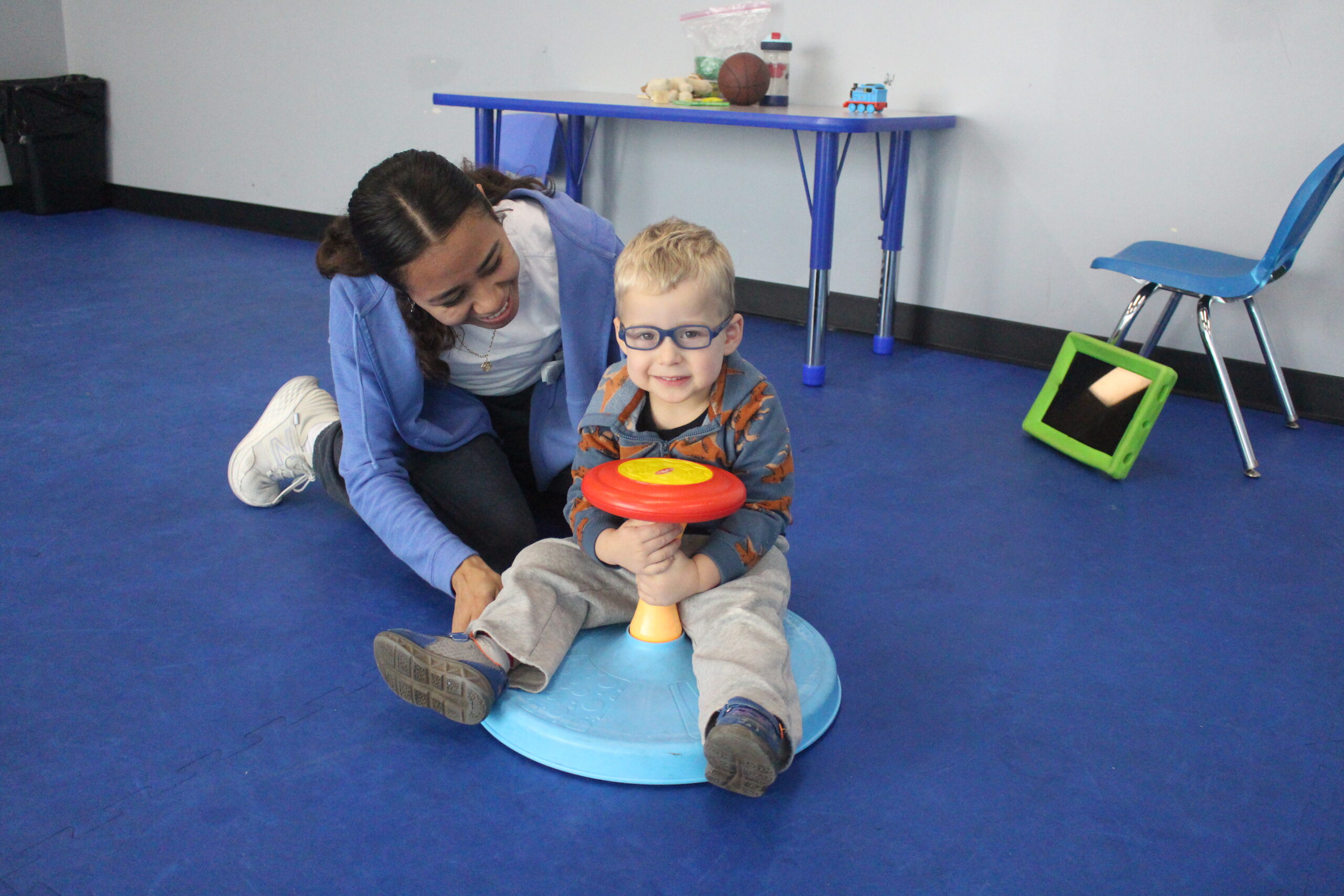 A therapy tech works with her client on the floor, both are smiling.